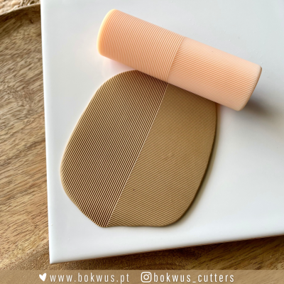 Rolo de silicone cor salmão e placa de massa bicolor com textura de linhas finas sobre superfície branca