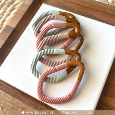 Seis moldes cortantes para biscoitos em forma de pássaro coloridos, sobre tabuleiro branco e fundo de madeira