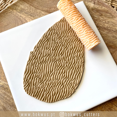 Massa marrom clara com textura ondulada e rolo texturizador alaranjado sobre placa branca