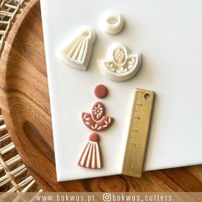 Cortadores de massa branca em formas florais e peças vermelhas moldadas, com régua dourada sobre superfície branca e tabuleiro de madeira.