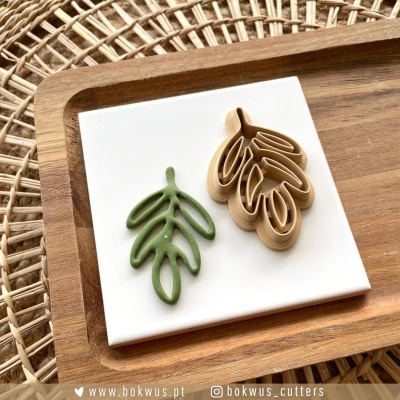 Cortadores de biscoito em forma de folhas sobre placa branca dentro de bandeja de madeira