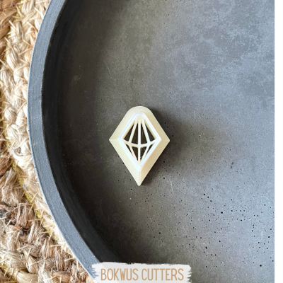 Cortador de bolachas losango branco com padrão geométrico numa tigela preta