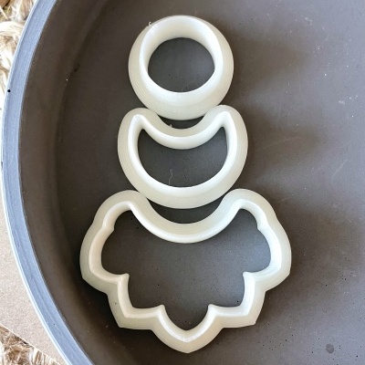 Três cortadores de biscoito brancos de plástico em diferentes formatos sobre prato cinza