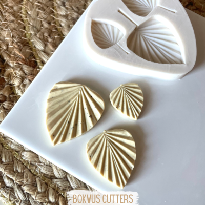 Moldes de silicone branco e peças de argila em forma de folhas sobre tábua branca com fundo de tecido de palha