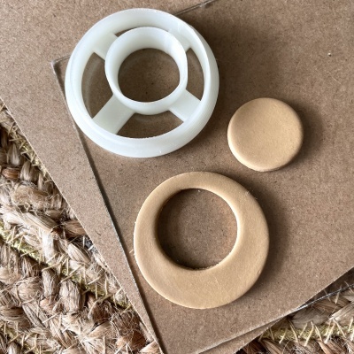 Três peças circulares feitas de plástico branco e material bege colocadas sobre cartão e tapete de fibras naturais