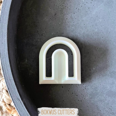 Cortador de bolachas em formato de arco branco sobre superfície cinza escura rugosa