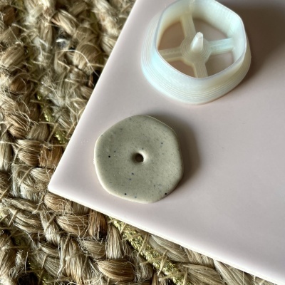 Botão cinza claro com manchas pretas ao lado de objeto plástico branco numa superfície rosa sobre tecido de corda entrelaçada