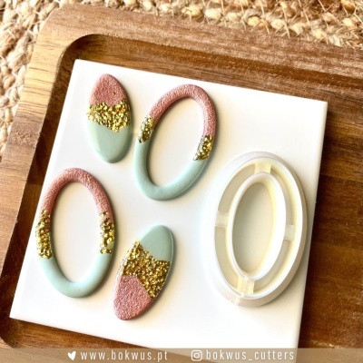 Moldes para joalharia ovais em rosa, verde claro e dourado sobre placa branca em madeira