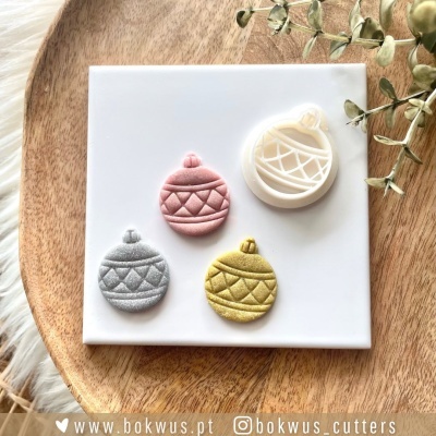 Cortadores de biscoitos em forma de bola de Natal sobre placa branca e bandeja de madeira