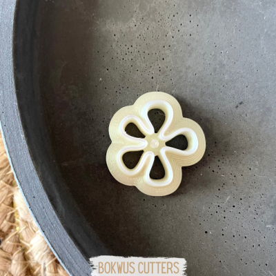 Cortador de massa em forma de flor branca sobre prato escuro