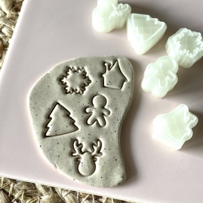 Massa cinzenta com formas de Natal cortadas ao lado de cortadores de plástico branco