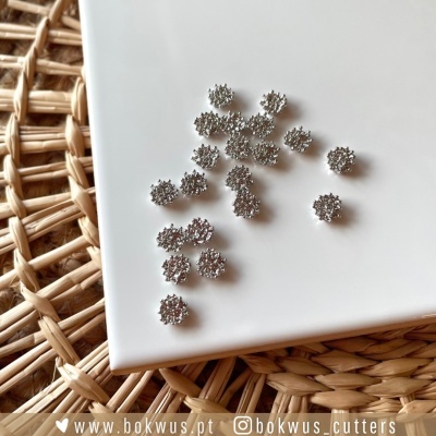 Peças metálicas pequenas prateadas texturizadas em placa branca sobre rattan, com texto www.bokwus.pt @bokwus_cutters