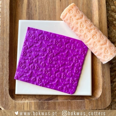Moldes de corte para confeitaria com padrões em relevo em silicone com cores pêssego e roxo sobre bandeja de madeira