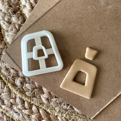 Cortador de plástico branco e peça de massa beige moldada em forma de alça de bolsa sobre cartão castanho e tapete de fibra.