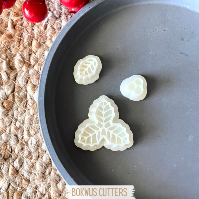 Três cortadores de biscoito em plástico branco com formas de folhas numa superfície cinzenta redonda