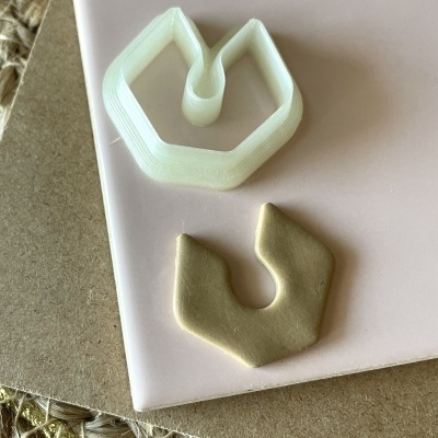 Cortador de massa branco em forma geométrica e massa bege moldada em forma similar sobre superfícies rosa, castanha e tecido trançado