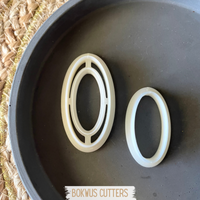 Dois cortadores de massa ovais brancos em placa preta, cartão BOKWUS CUTTERS
