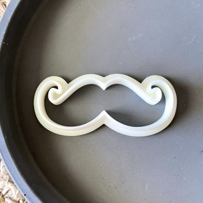 Molde de plástico branco em forma de bigode sobre superfície redonda cinza