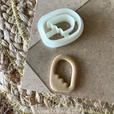 Cortador de massa branco e peça de massa cortada castanha clara sobre cartão e tapete de fibras naturais.