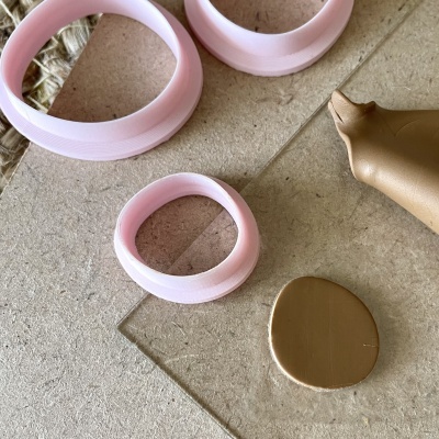 Moldes plásticos circulares rosa claros, massa dourada oval e em cone, sobre superfície cinza.