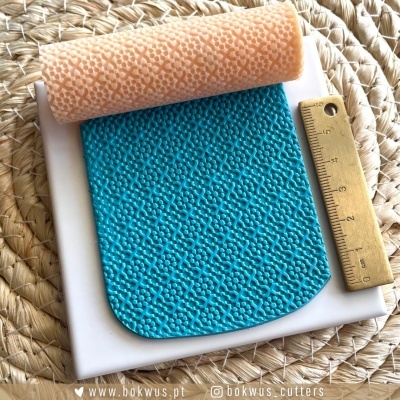 Rolo de textura cor de pêssego e tapete de silicone azul com padrão granular, régua dourada, base branca e tapete de fibras naturais