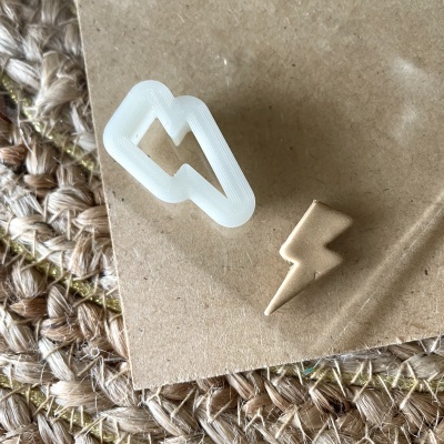 Corta-massa branco em forma de raio e biscoito dourado em forma de raio sobre cartão e tapete trançado