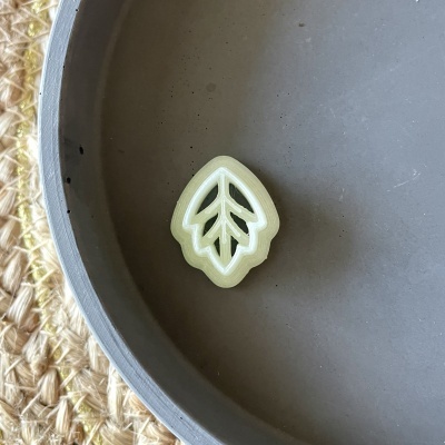 Botão em forma de folha verde claro sobre prato cinzento fosco e tecido de juta.