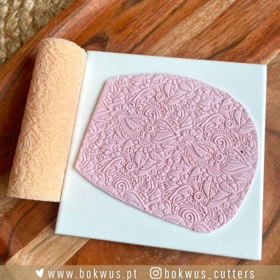 Rolo texturizador creme com padrão floral e pasta rosa texturizada sobre base branca