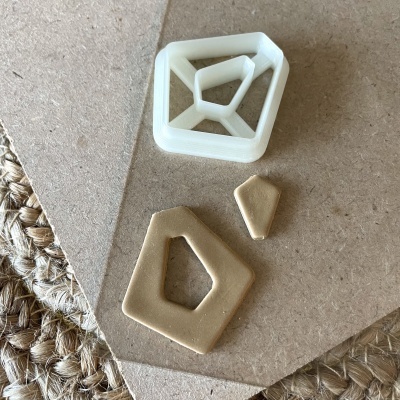 Cortador branco de plástico em forma geométrica e peça cortada em massa bege sobre cartão e tapete de corda