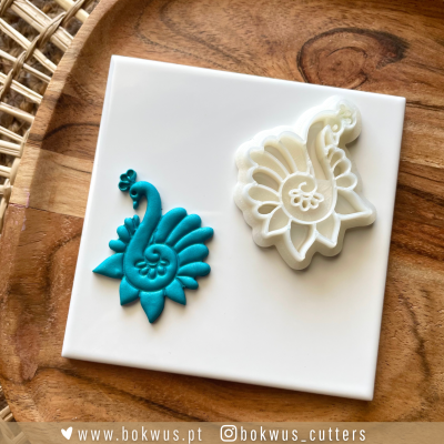 Cortador de plástico branco e peça decorativa azul turquesa sobre base branca e superfície de madeira.