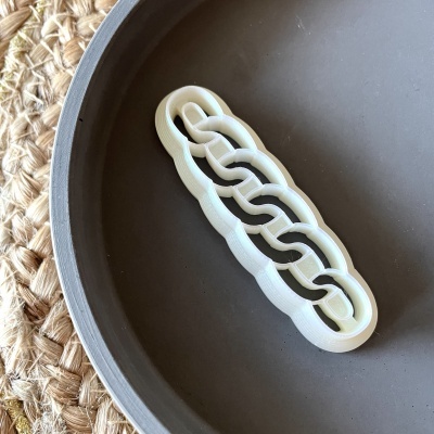 Presilha de cabelo branca em elos sobre prato cinzento e tecido trançado