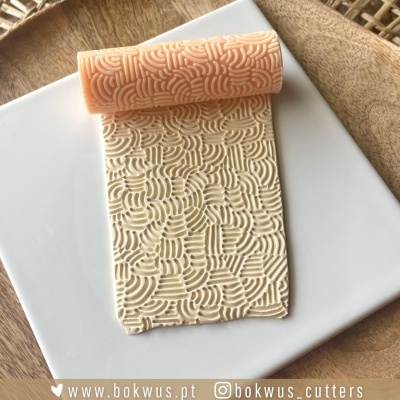 Rolo texturizador laranja com padrão de linhas curvas sobre massa creme em prato branco