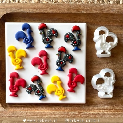 Cortadores e peças decorativas em forma de galo coloridas e de plástico, numa base branca sobre madeira