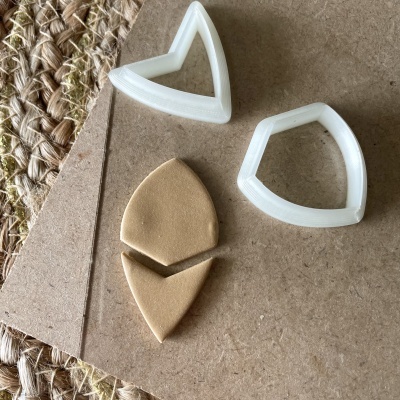 Cortadores brancos de plástico e massa bege cortada em forma de escudo sobre superfície castanha e tapete de fibras naturais