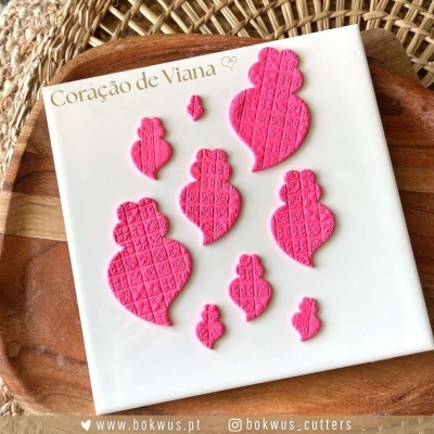 Recortes rosa de Coração de Viana em cartão branco, sobre área de madeira e rattan.