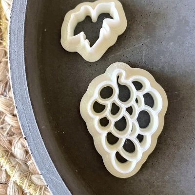 Dois cortadores de biscoitos em forma de uvas e folha em tigela cinza