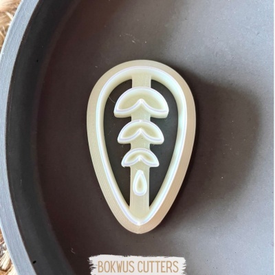 Cortador de bolachas branco em forma de gota com folhas, numa superfície cinzenta escura