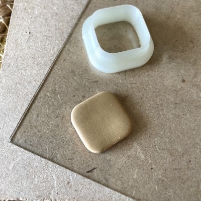 Duas peças quadradas pequenas em plástico branco e castanho sobre superfície bege com tapete de fibras naturais