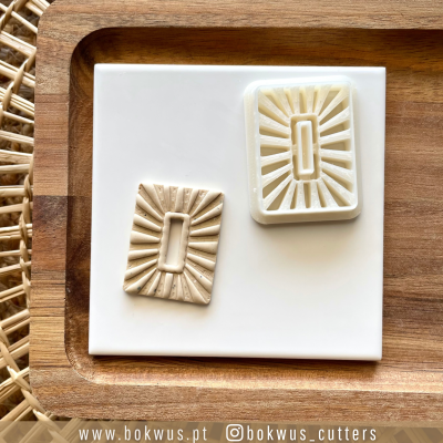Dois cortadores retangulares com padrão de raios solares sobre bandeja de madeira e placa branca