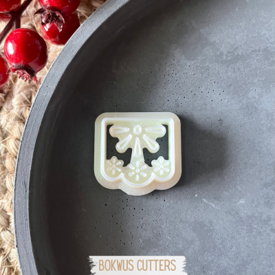 Cortador de bolos branco com desenho de laço e flores sobre prato cinzento e bagas vermelhas