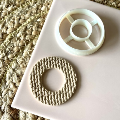 Dois moldes circulares, branco estruturado e bege texturizado, sobre superfície rosa e tapete de fibras trançadas