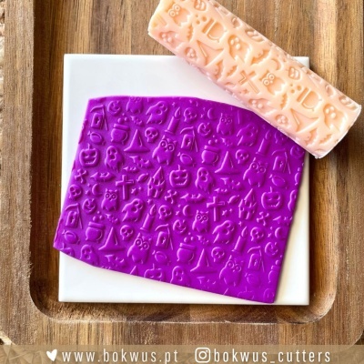 massa roxa e um rolo cor de pêssego com padrões em relevo de Halloween sobre superfície branca e tabuleiro de madeira