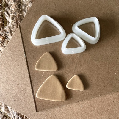 Cortadores triangulares brancos e pedaços de argila bege sobre papel castanho e tecido