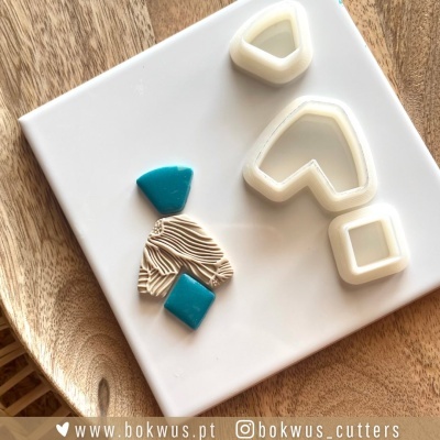 Cortadores de massa branca e pedaços de massa azul e bege sobre placa branca e madeira