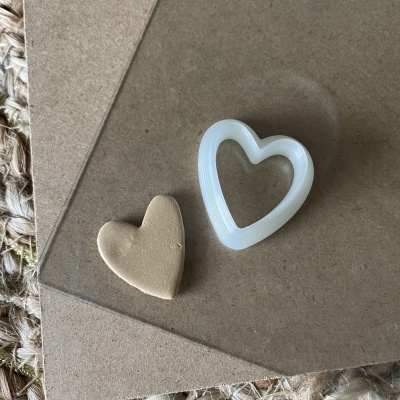 Cortador de biscoitos branco em forma de coração e massa de biscoito bege no formato de coração sobre papel castanho.