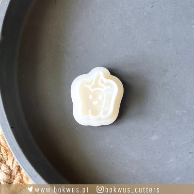 Cortante branco em forma de pimenta sobre superfície cinza.