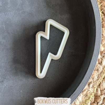 Cortador de biscoitos branco em forma de raio numa tigela cinzenta em cima de superfície de palha