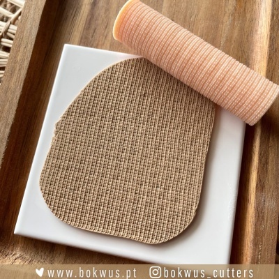 Rolo texturizador laranja e placa branca com textura quadriculada num suporte de madeira