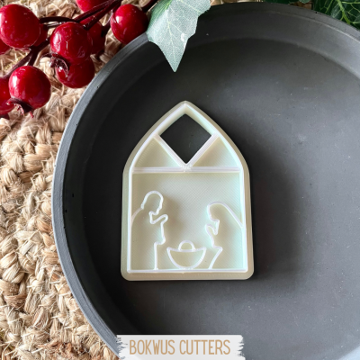 Cortador de bolachas branco em formato de casa com figuras humanas e berço, em prato preto, fundo rústico com bagas vermelhas e folhas verdes