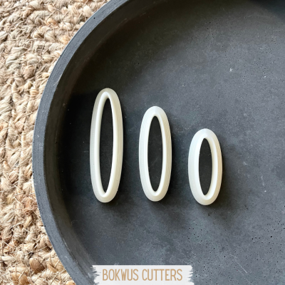 Três moldes ovalados brancos de tamanhos diferentes numa bandeja preta sobre base de fibra natural